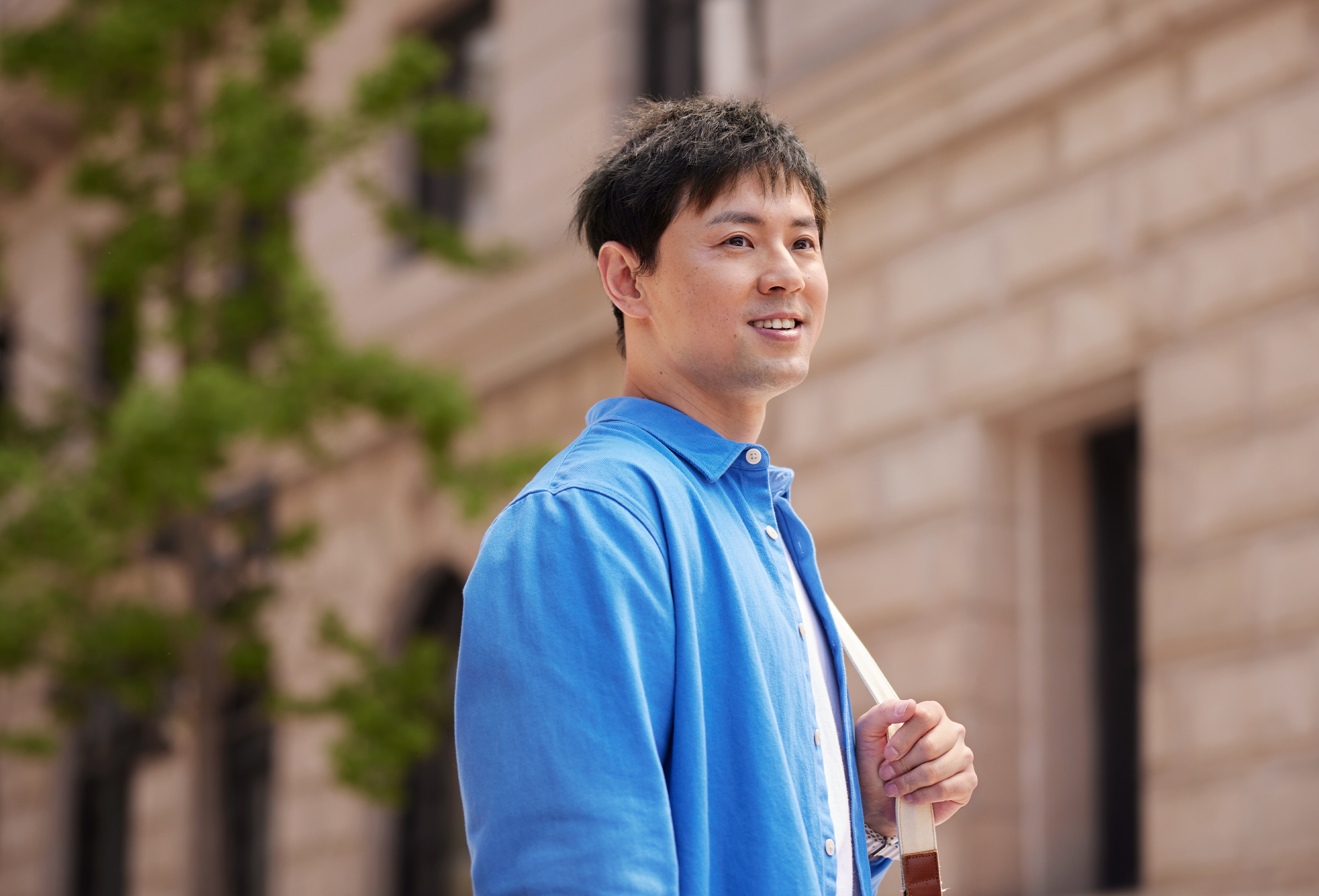 Apple 員工在磚牆辦公大樓外面帶微笑，拿著肩背袋。