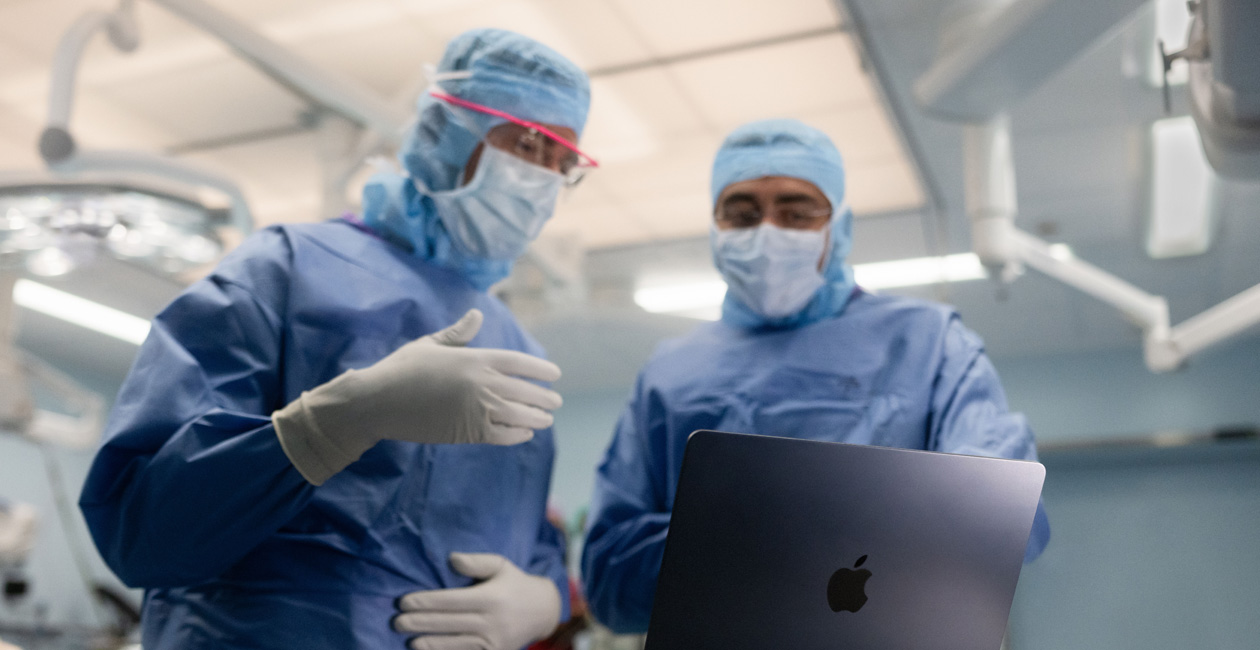 جراحان يناقشان أمراً على شاشة MacBook Pro في غرفة العمليات.