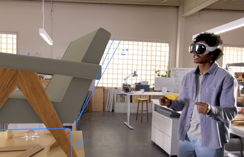 A designer wearing Apple Vision Pro uses hand movements to measure a 3D projection of a chair.
