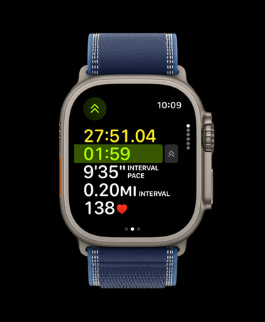Apple Watch Ultra 3 med urkasse av naturlig titan og Trail Loop i blå/klarblå viser treningsmålinger under løping utendørs.