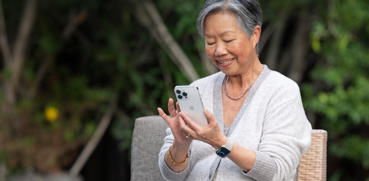 Một người phụ nữ lớn tuổi đang nhìn vào iPhone khi ngồi trên ghế. 