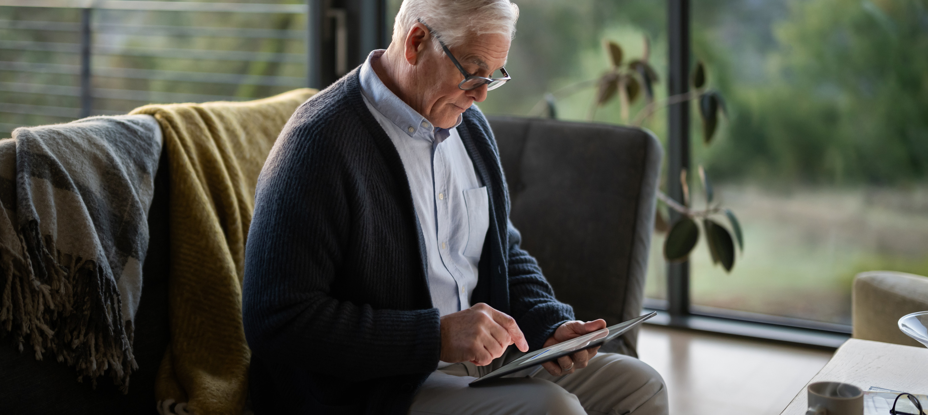Một người đàn ông lớn tuổi ngồi trên ghế sofa đang nhìn vào iPad.