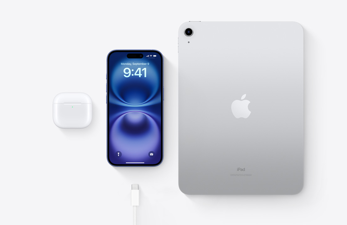 Pohled z ptačí perspektivy na AirPody Pro, iPhone 16 a iPad s konektorem USB‑C na ilustraci toho, že se všechna tři zařízení dají nabíjet stejným USB‑C kabelem.