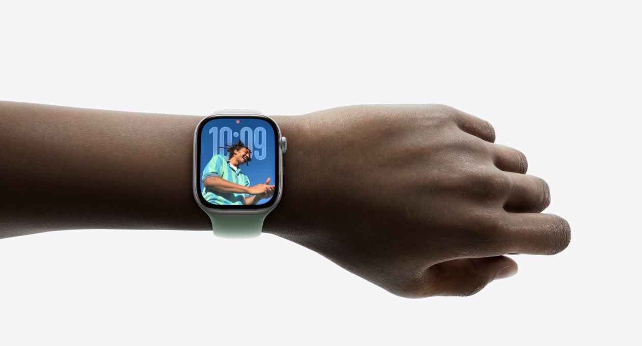 Nahaufnahme einer Apple Watch in Silber mit Gummiarmband am Handgelenk einer Person mit dem neuen Liquid Glass Design