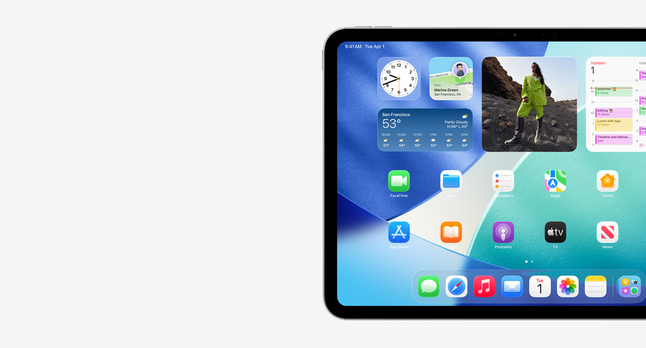 iPad, orientation paysage, côté gauche seulement, l’écran d’accueil affiche des widgets en pile, dont l’horloge translucide montrant l’effet Liquid Glass, l’app Localiser et le widget Météo, deux rangées d’apps plus petites et le Dock