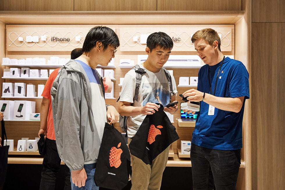 Een Apple medewerker helpt klanten met iPhone 14 in Apple Battersea.