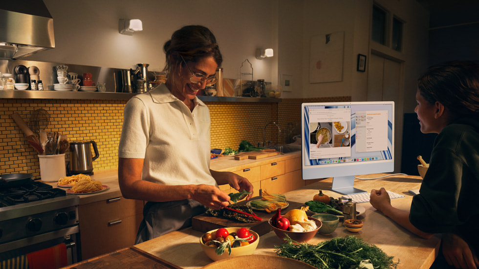 En forelder og et barn lager mat på kjøkkenet og bruker nye iMac med M3-chip i blå med tastatur og mus i matchende farge.