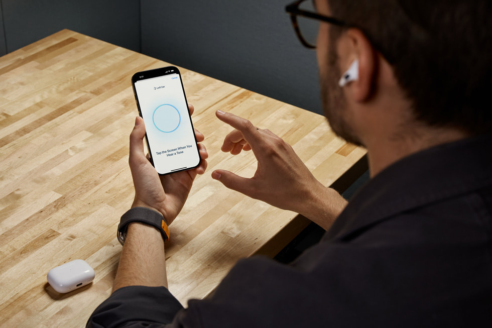 Osoba z założonymi AirPods Pro 2, która trzyma iPhone’a i korzysta z nowej funkcji Badanie słuchu.
