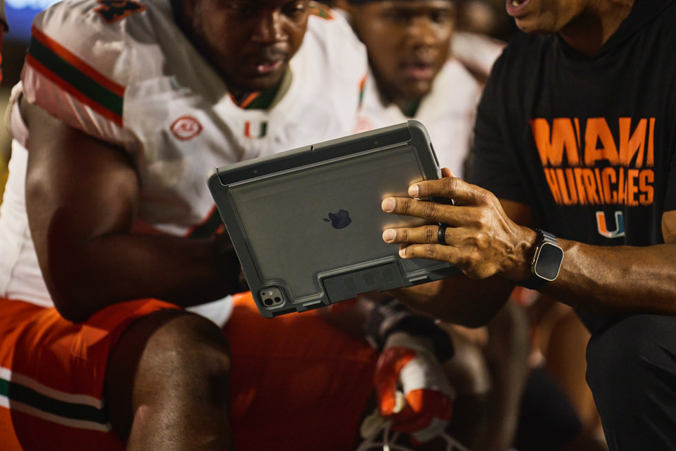 Un entraîneur de Miami visionne des images sur iPad avec des joueurs sur la ligne de touche pendant le match.
