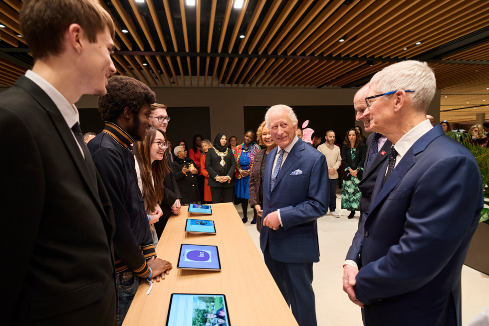 Le roi Charles et Tim Cook rencontrent des jeunes ayant bénéficié de l’aide de The King’s Trust et qui se tiennent en arrière d’une table où sont disposés des iPad.