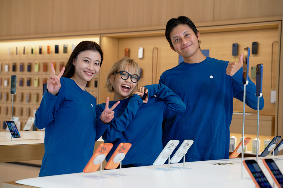 Apple 銀座のiPhoneのディスプレイの前でポーズを取る3人のチームメンバー。
