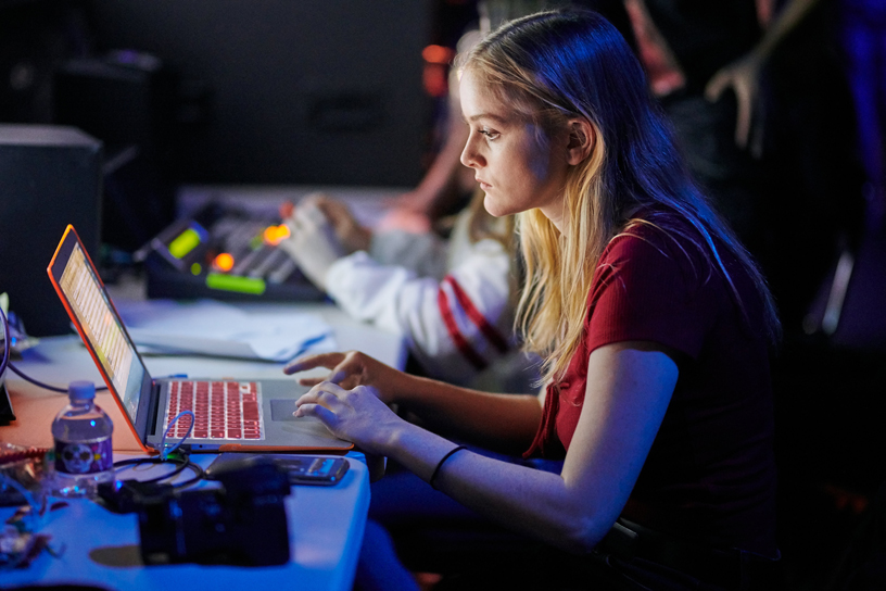 Un estudiante de producción trabaja con la computadora detrás del escenario.