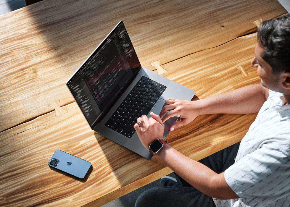 لقطة علوية تظهر سوبنيل ساهاي يعمل على مكتب باستخدام جهاز MacBook Pro، وiPhone بجانبه.
