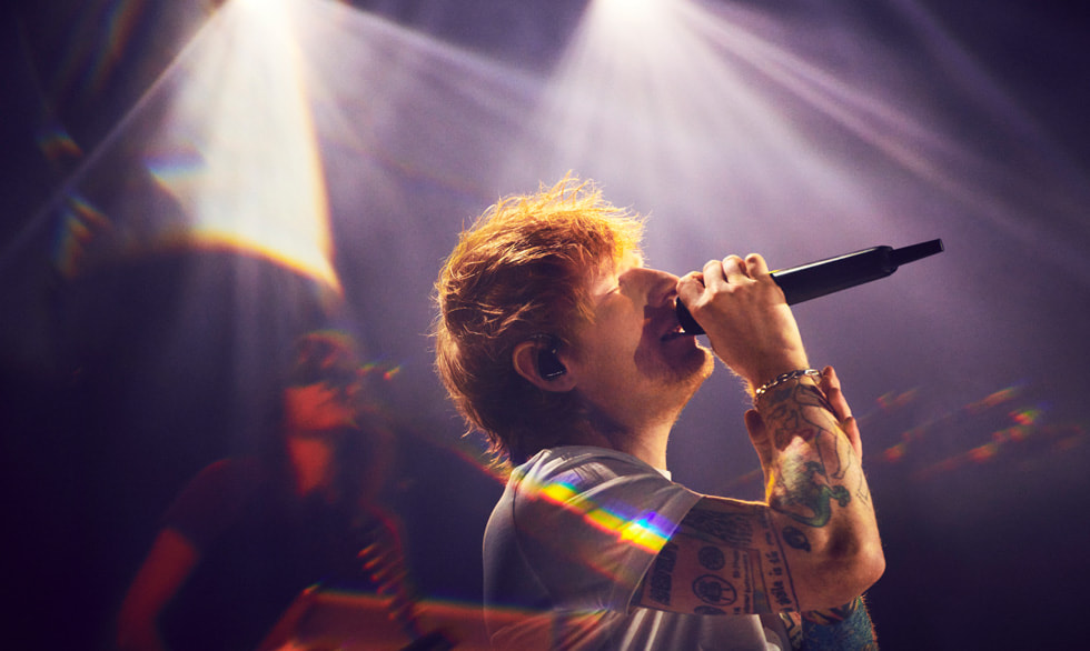 Sångaren och låtskrivaren Ed Sheeran står på scenen och sjunger i en mikrofon.