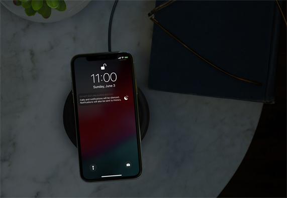 Karanlık bir odada, kablosuz şarj cihazında duran iPhone, Rahatsız Etme modunda. 